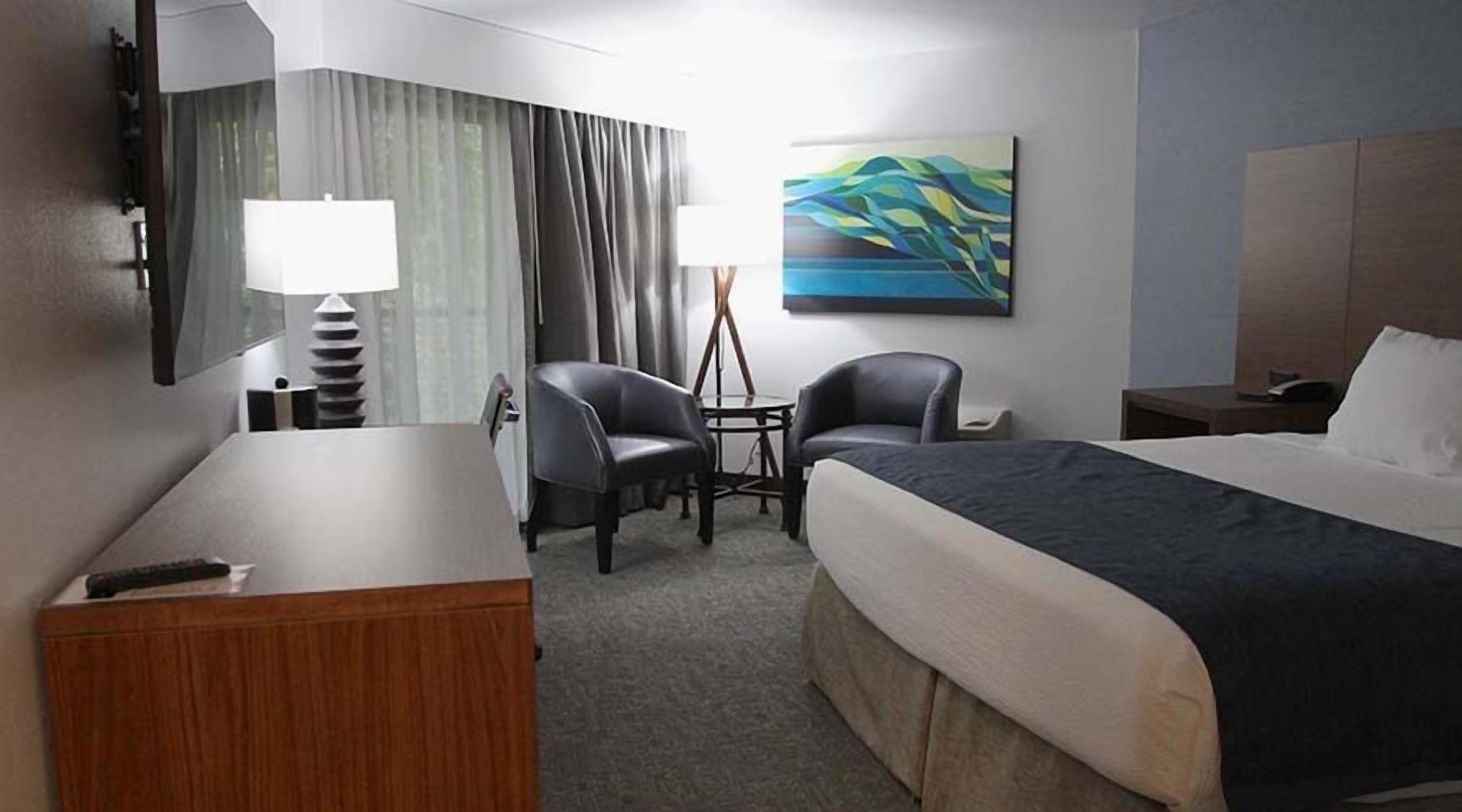 Et hotelværelse med en seng, to stole, et skrivebord, en lampe, et billede og udsigt til det fri.