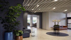 Een moderne lobby met een grote potplant, een ronde tafel met bloemen en een zithoek met een bank en stoelen.
