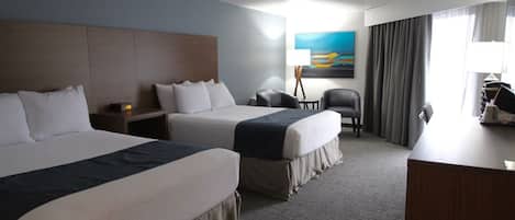 Ett hotellrum med två sängar, ett skrivbord, en stol, en lampa och en tavla på väggen.