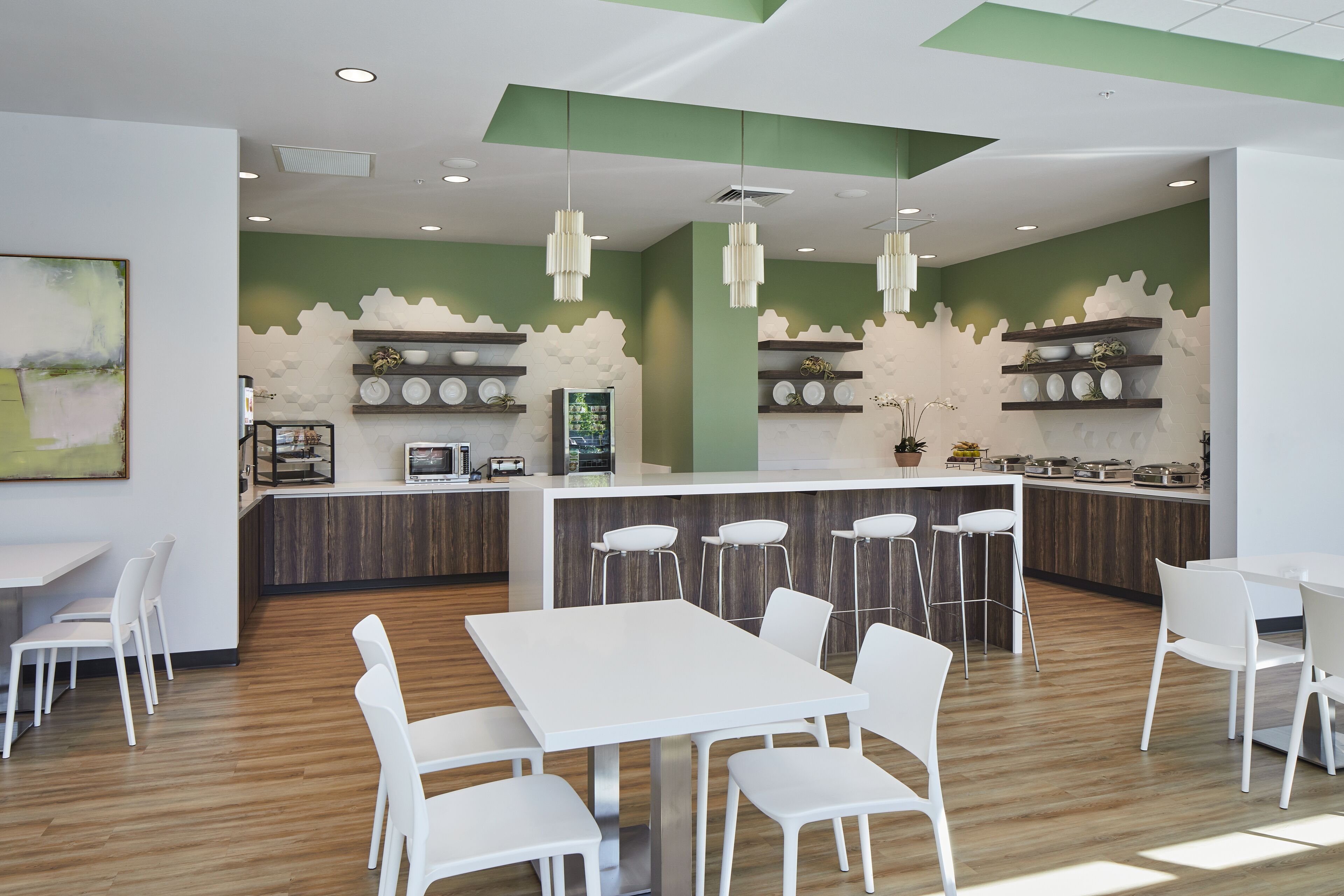 A modern kitchen with white bar stools, a central island, and a green accent wall.