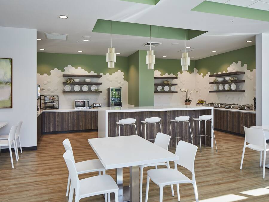 A modern kitchen with white bar stools, a central island, and a green accent wall.