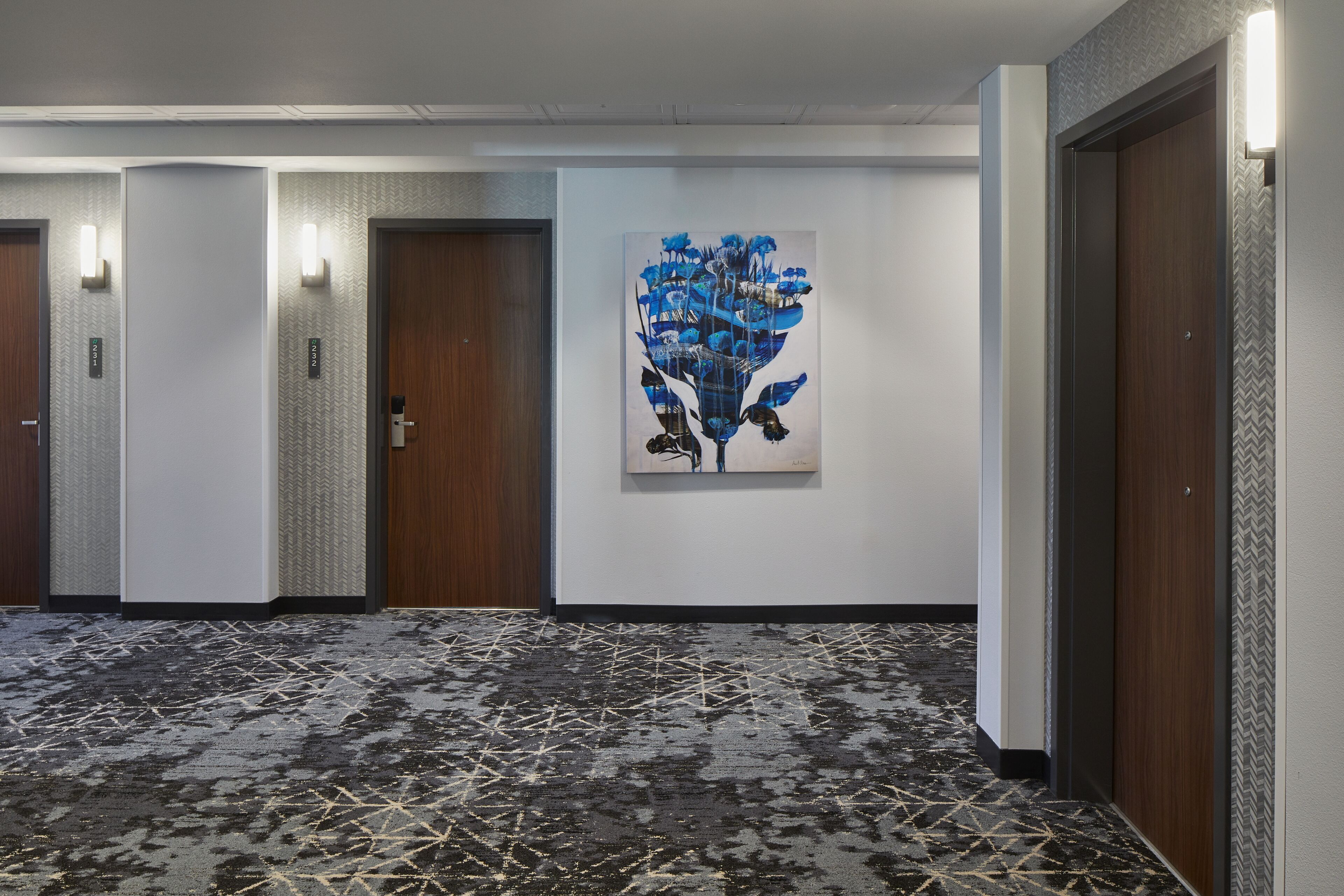 Un couloir avec un tapis à motifs, une grande peinture abstraite accrochée au mur et des portes en bois.