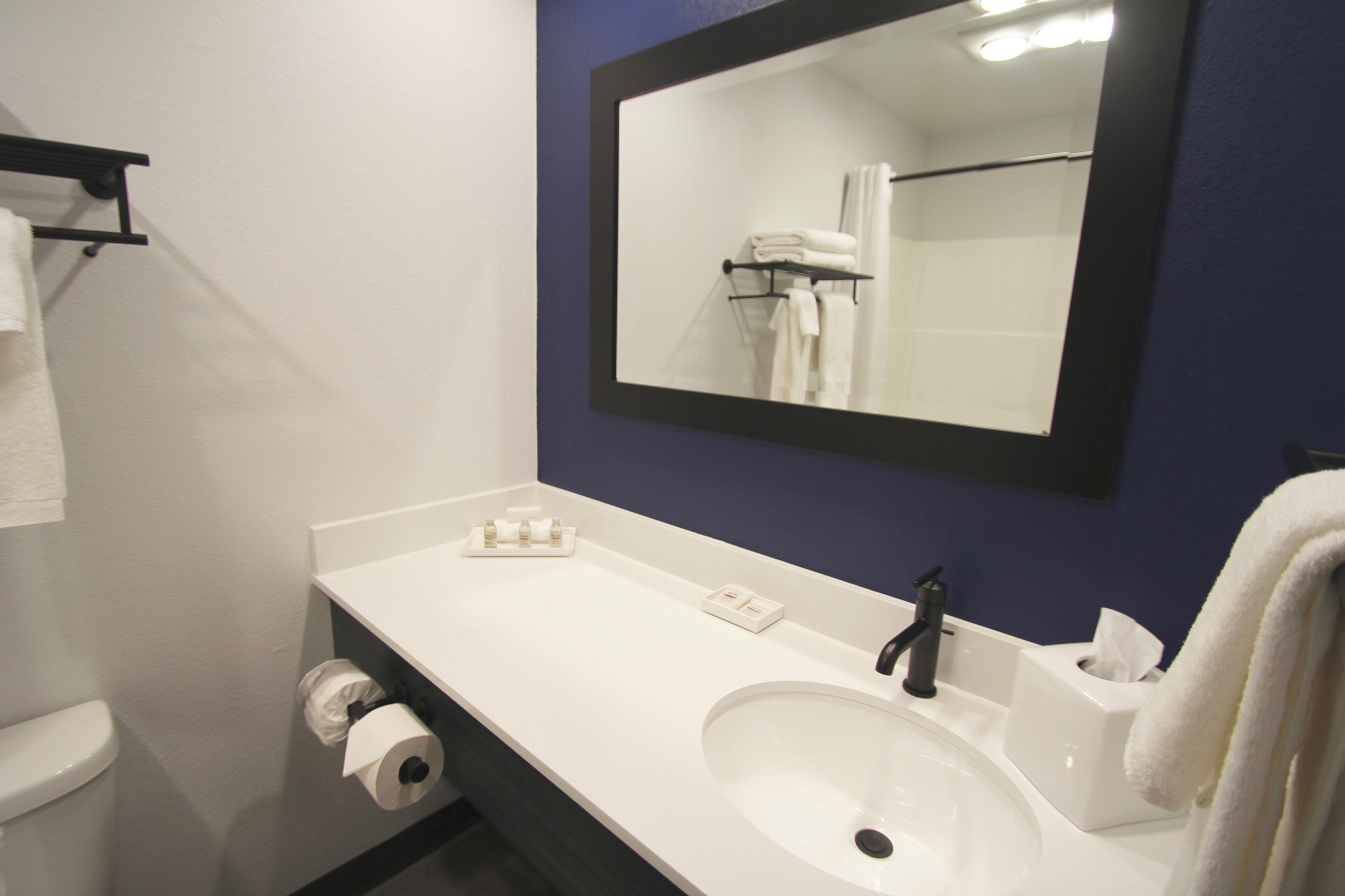 Un baño con lavamanos blanco, espejo, toallero y retrete.