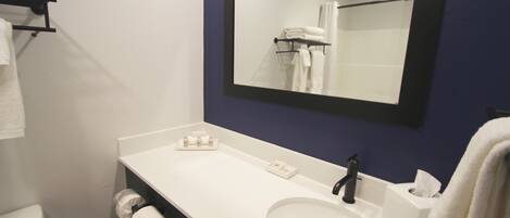 Un baño con lavamanos blanco, espejo, toallero y retrete.
