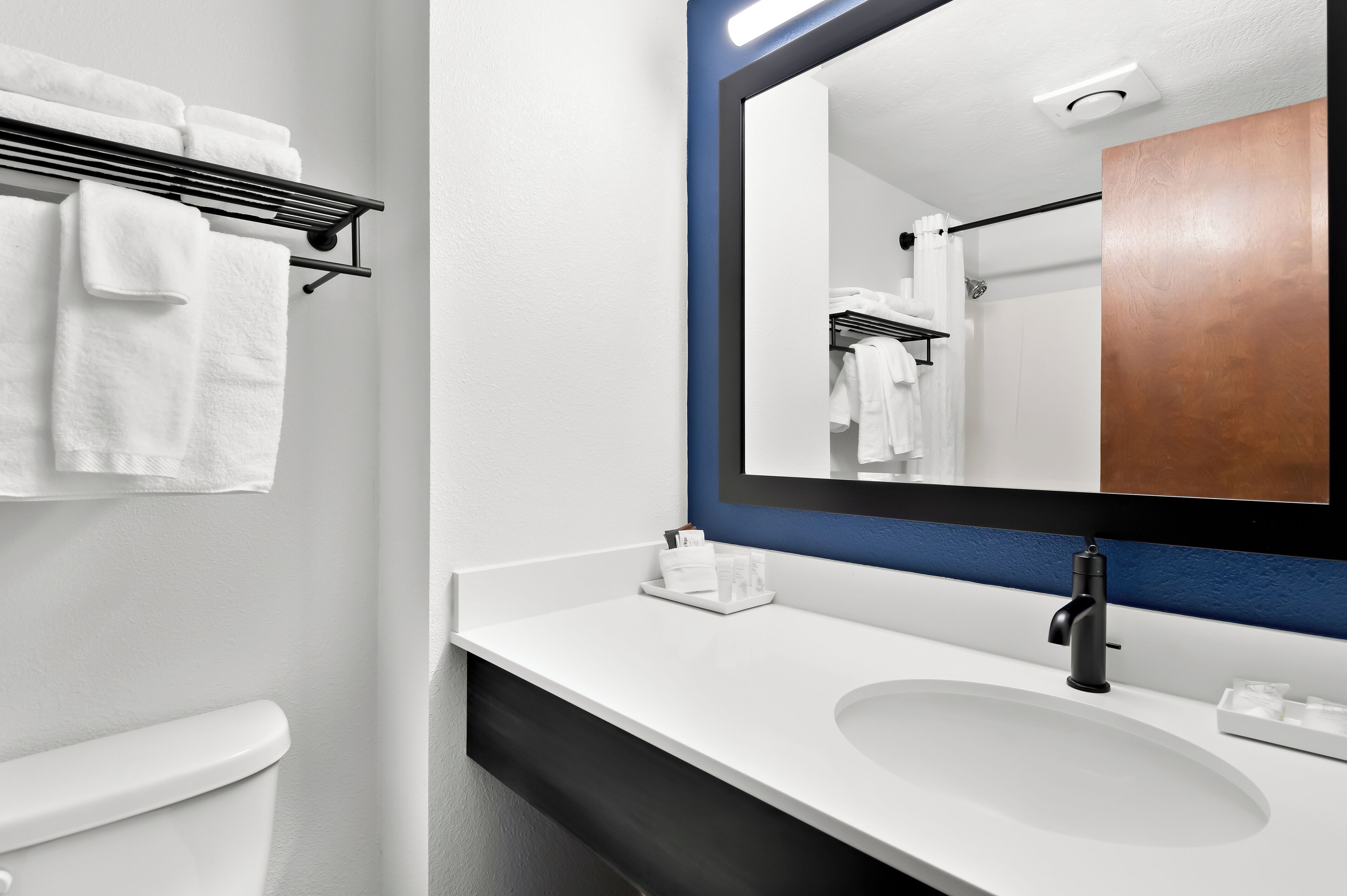 Un baño moderno con un lavamanos blanco, un grifo negro y un espejo grande con marco de madera.