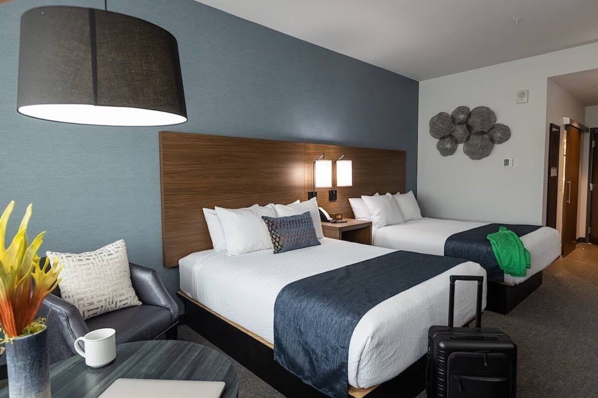 A hotel room with two beds, a desk, a chair, a lamp, and a decorative wall piece.