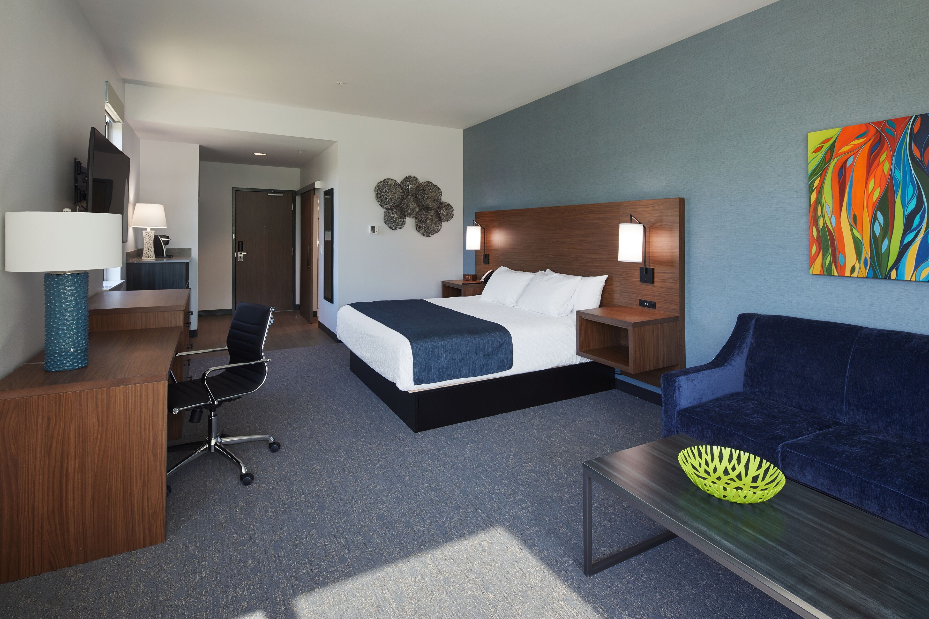 A hotel room with a bed, a desk, a chair, a sofa, and a wall art piece.