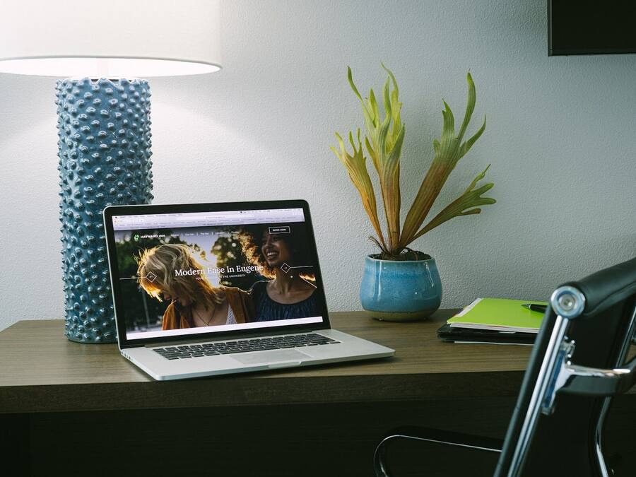 Una computadora portátil sobre un escritorio, con un florero azul y una planta en maceta.