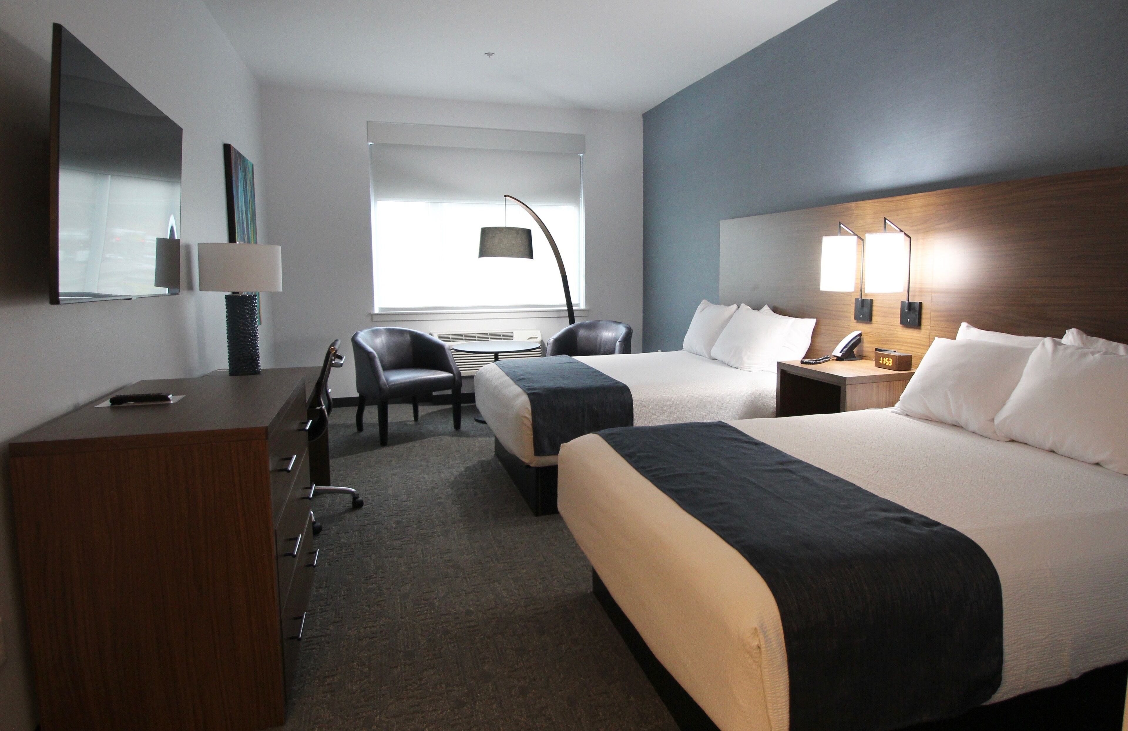 A hotel room with two beds, a desk, a chair, a lamp, and a large window.