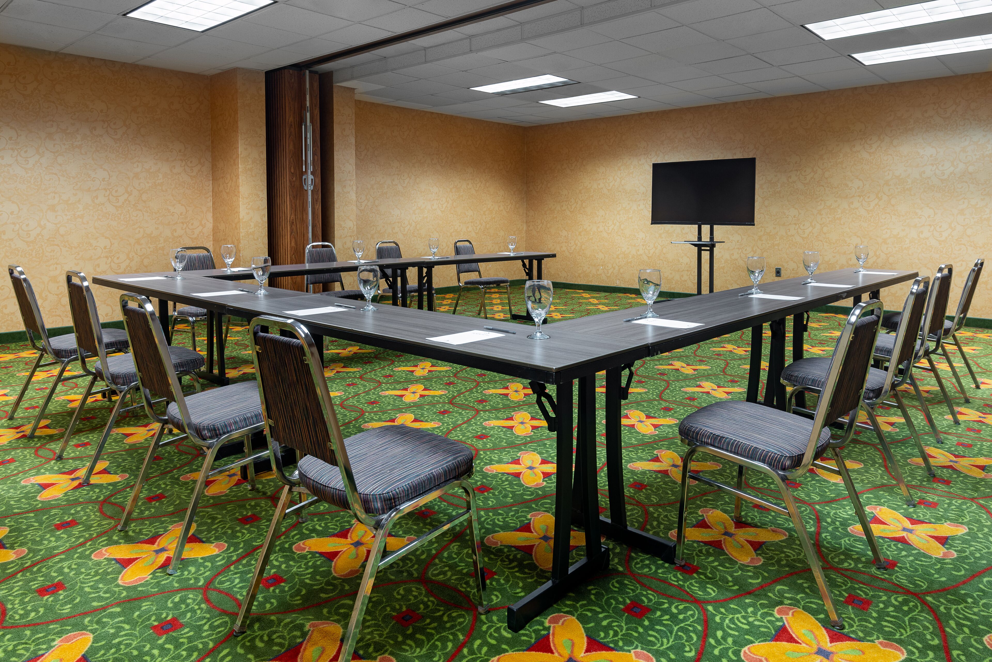 A conference room with a long table, chairs, a screen, and a carpet with a floral pattern.