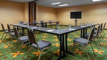 A conference room with a long table, chairs, a screen, and a carpet with a floral pattern.