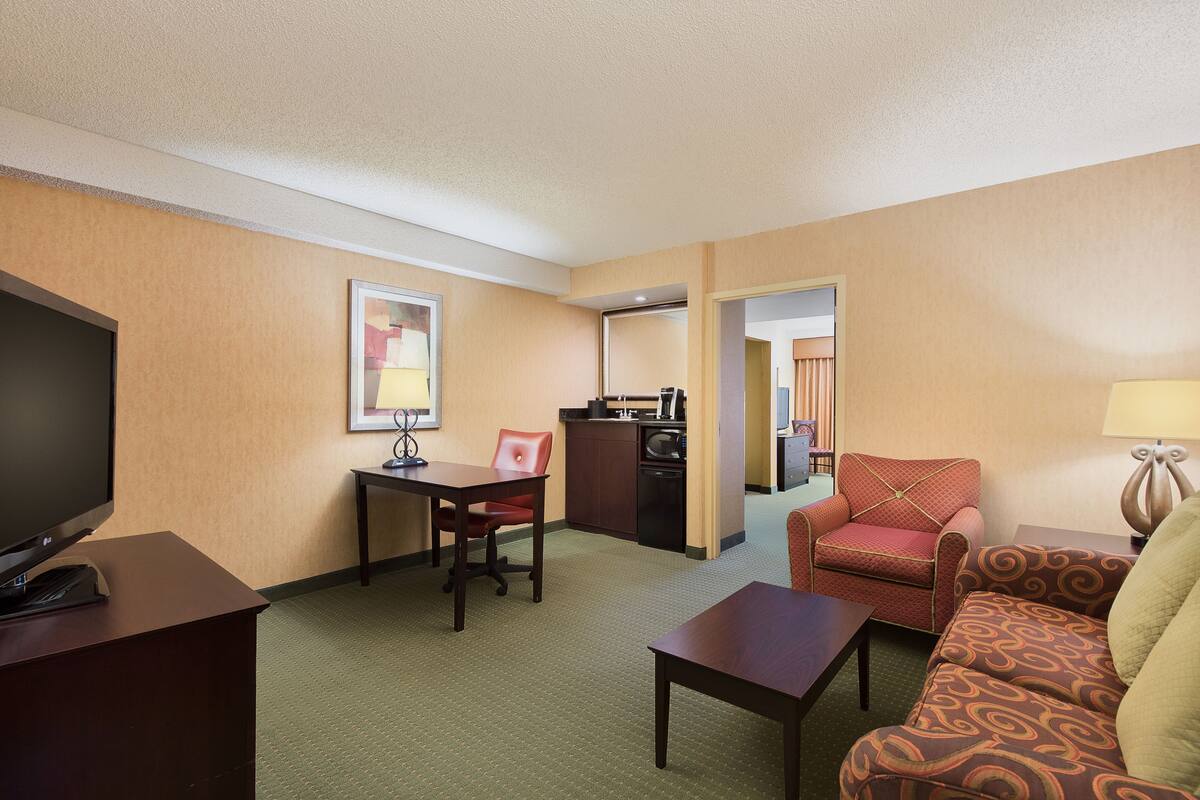 A hotel room with a television, a dining table, a sofa, and a kitchenette.