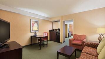 A hotel room with a television, a dining table, a sofa, and a kitchenette.