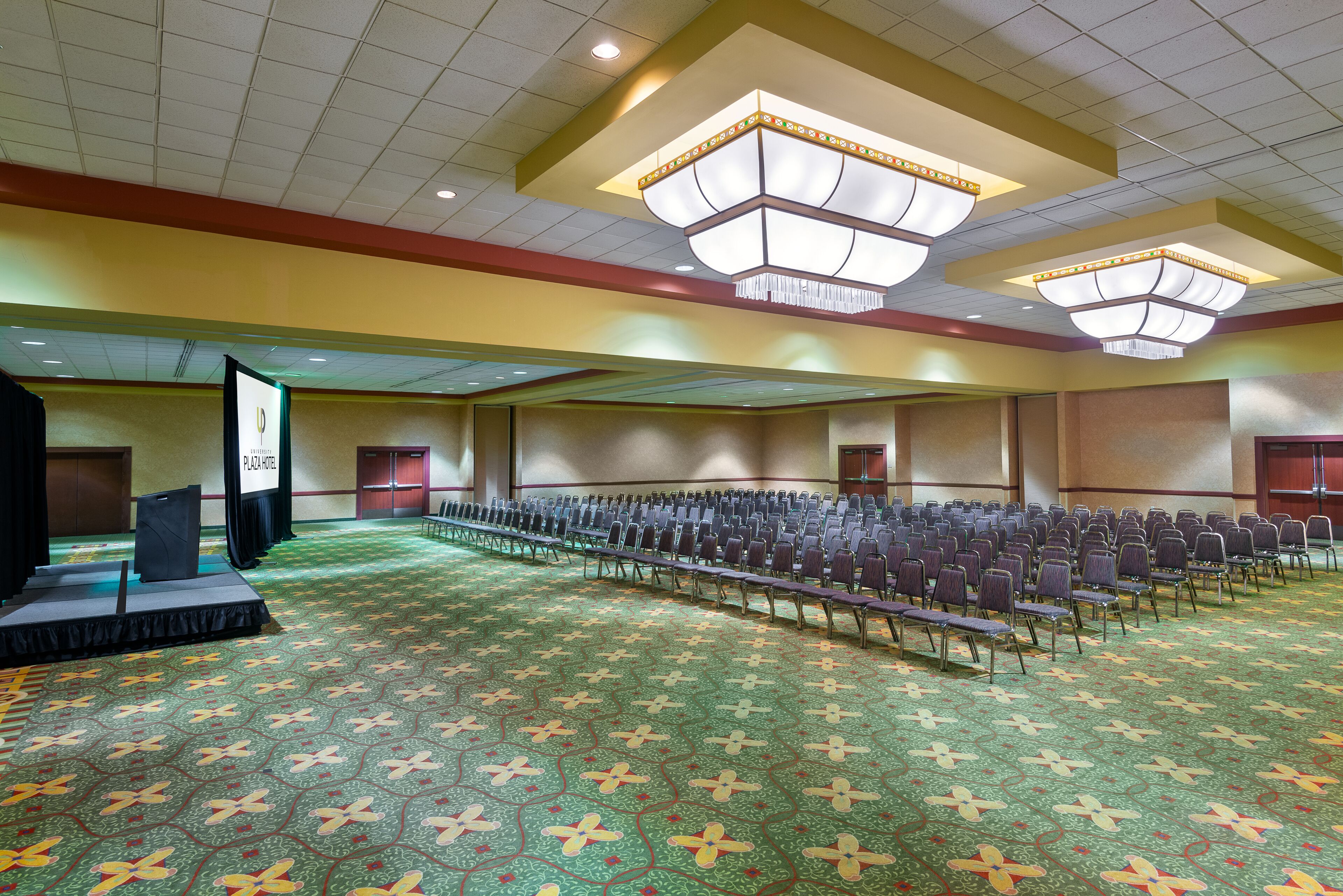 A large conference room with rows of chairs, a stage, and a carpeted floor.