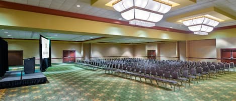 Un salón de conferencias amplio con filas de sillas, un escenario y piso alfombrado.