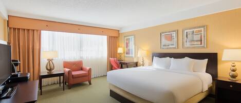 A hotel room with a large bed, a desk with a lamp, a chair, and a television.