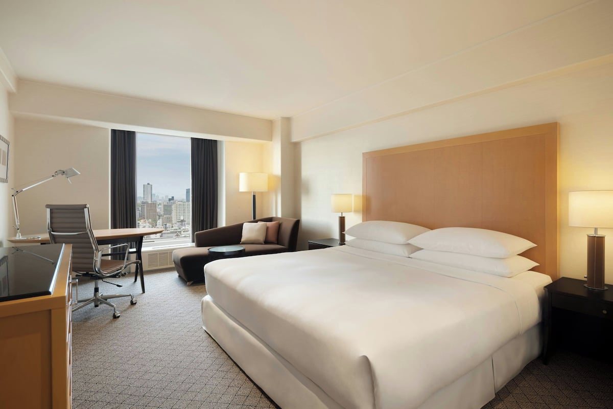 A hotel room with a large bed, a desk with a chair, a sofa, and a view of the city.