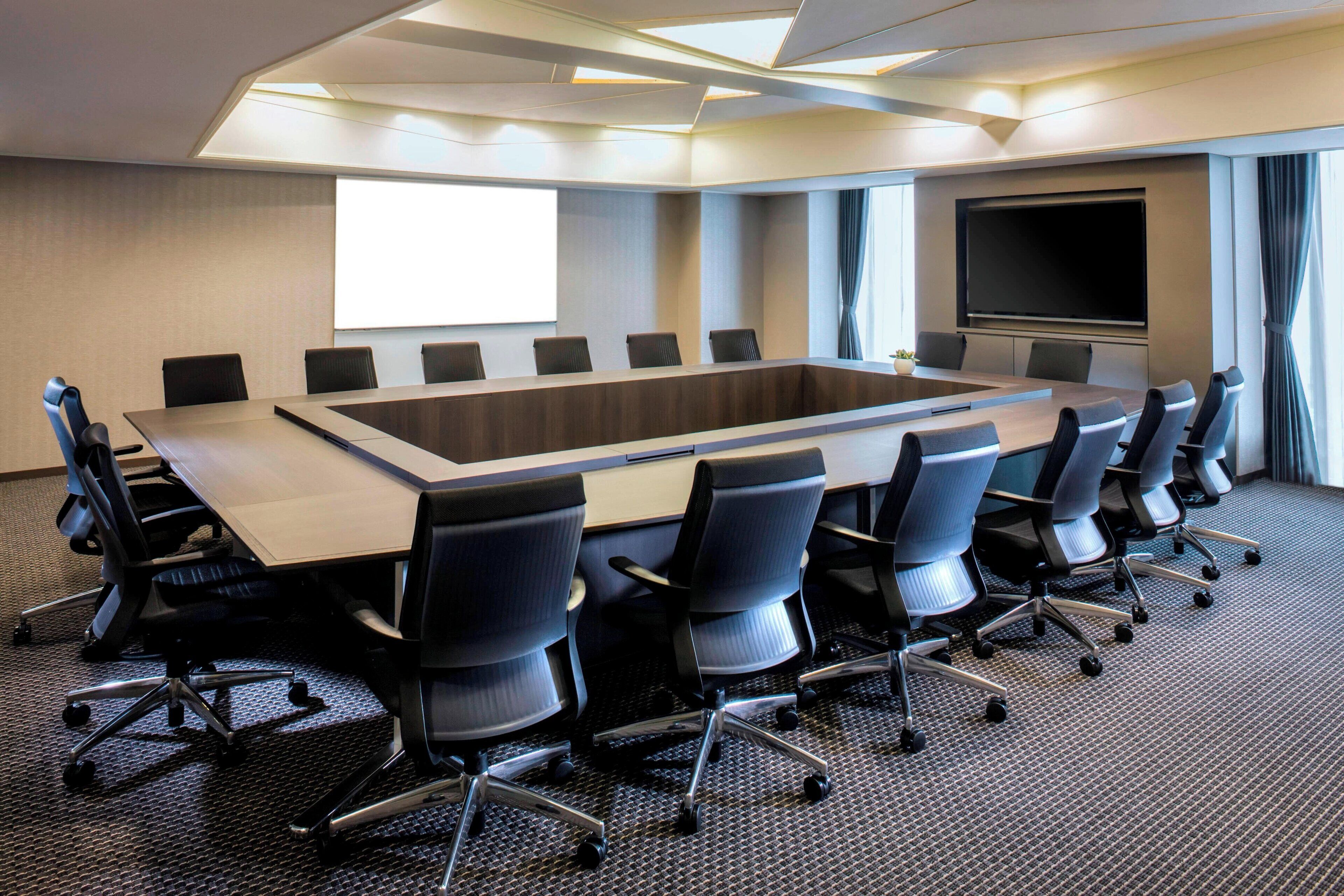 A conference room with a long table, black chairs, a large screen, and a projector.