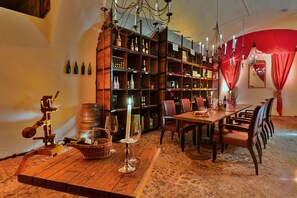 Un comedor con una mesa de madera, sillas y una estantería para vinos con botellas.
