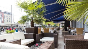 An outdoor seating area with wicker furniture and a palm tree. - Hotel Euler (Basel)