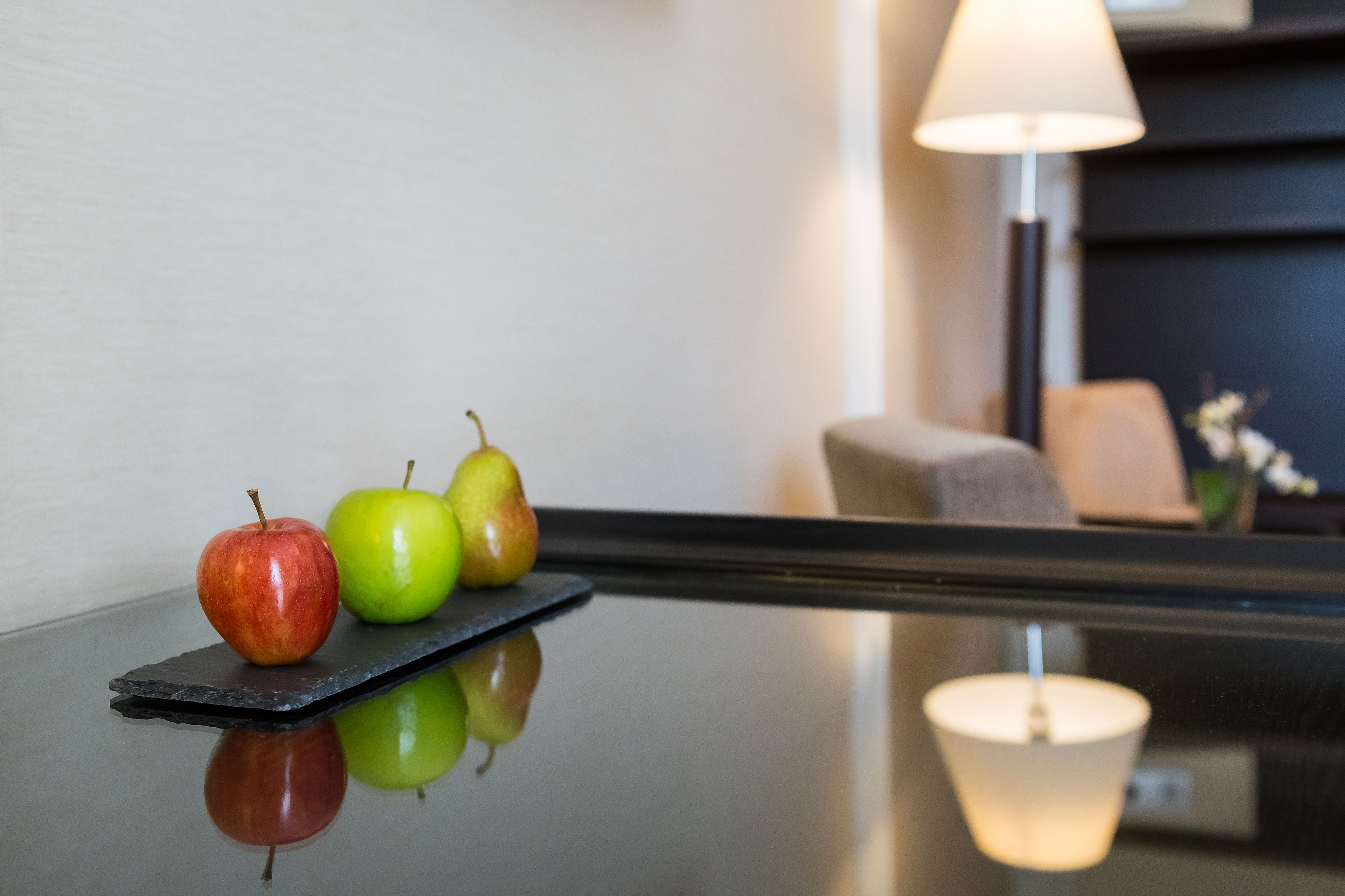 A polished table with three apples and a lamp in the background.