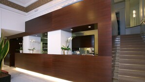 A reception desk with a modern design, flanked by potted plants and a staircase. - Hotel Euler (Basel)