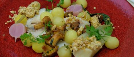 A red plate with a seafood dish, including fish, mushrooms, and garnishes.