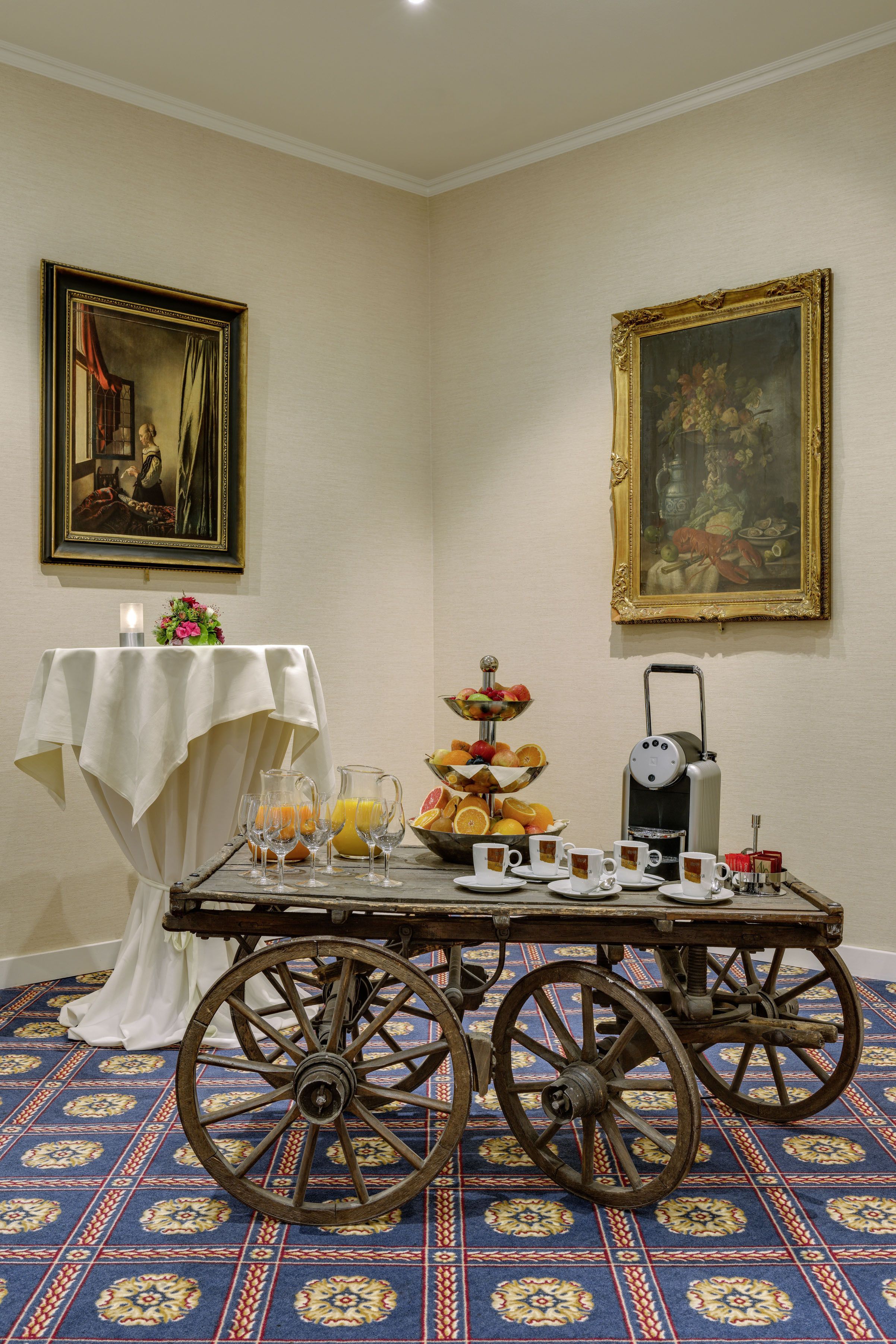 A dining table with a white tablecloth, fruit bowl, pitcher, cups, and a coffee maker.