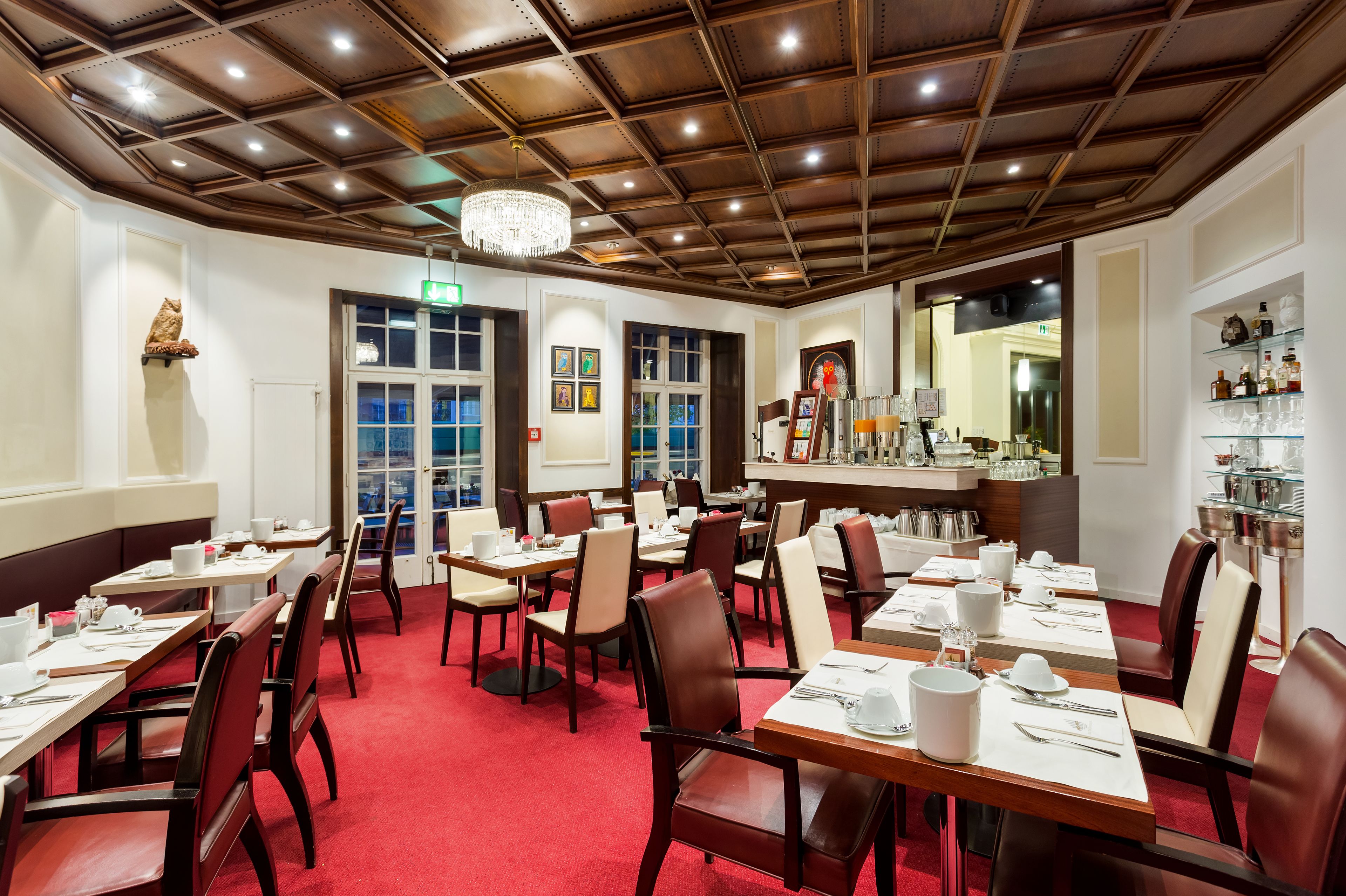 Un espace repas avec des tables dressées pour le service, un bar bien garni de bouteilles variées et un lustre.