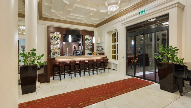 A lobby with a bar area, a red carpet, and a glass door entrance. - Hotel Euler (Basel)