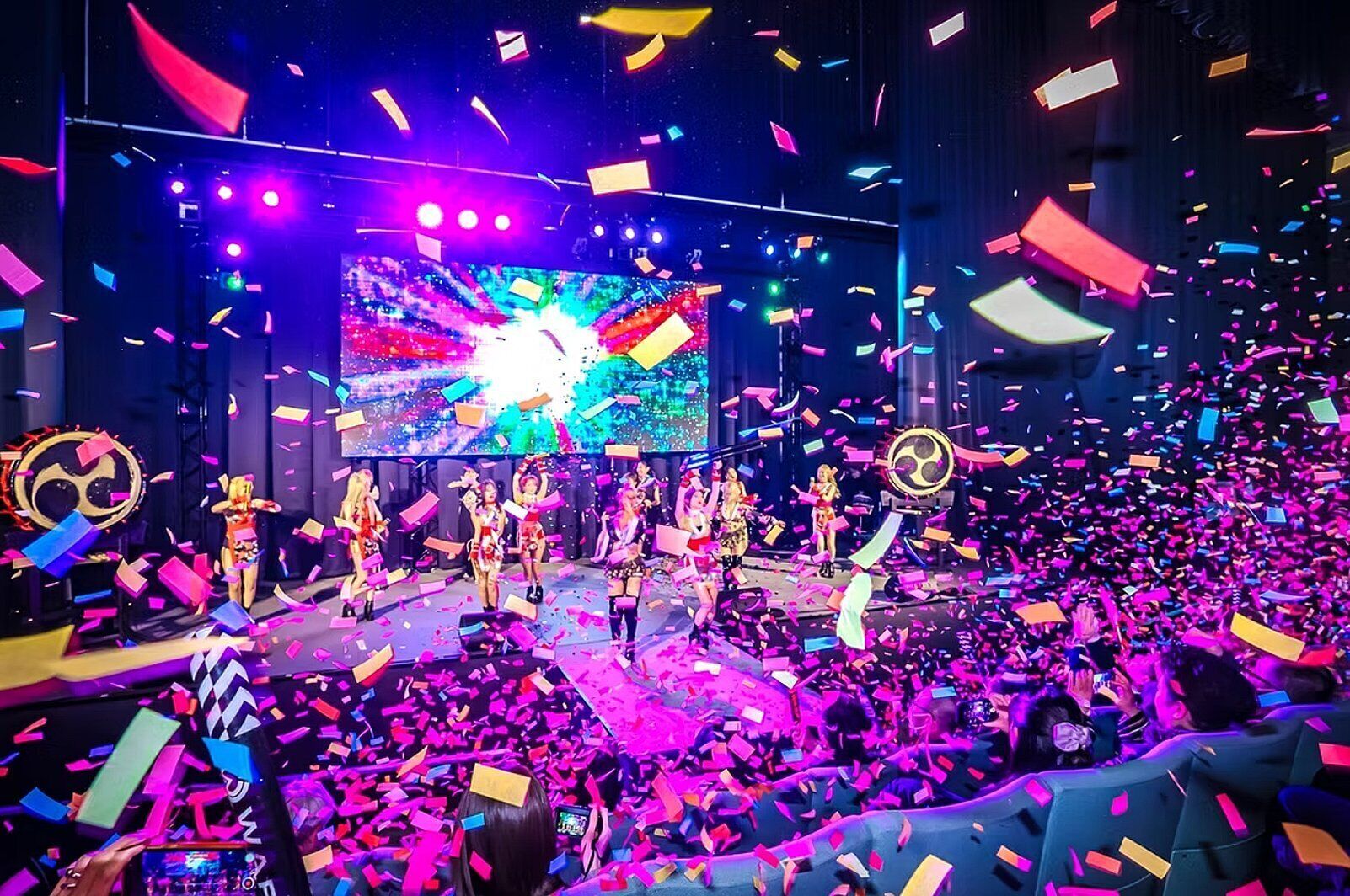 A stage with performers and confetti, surrounded by an audience.
