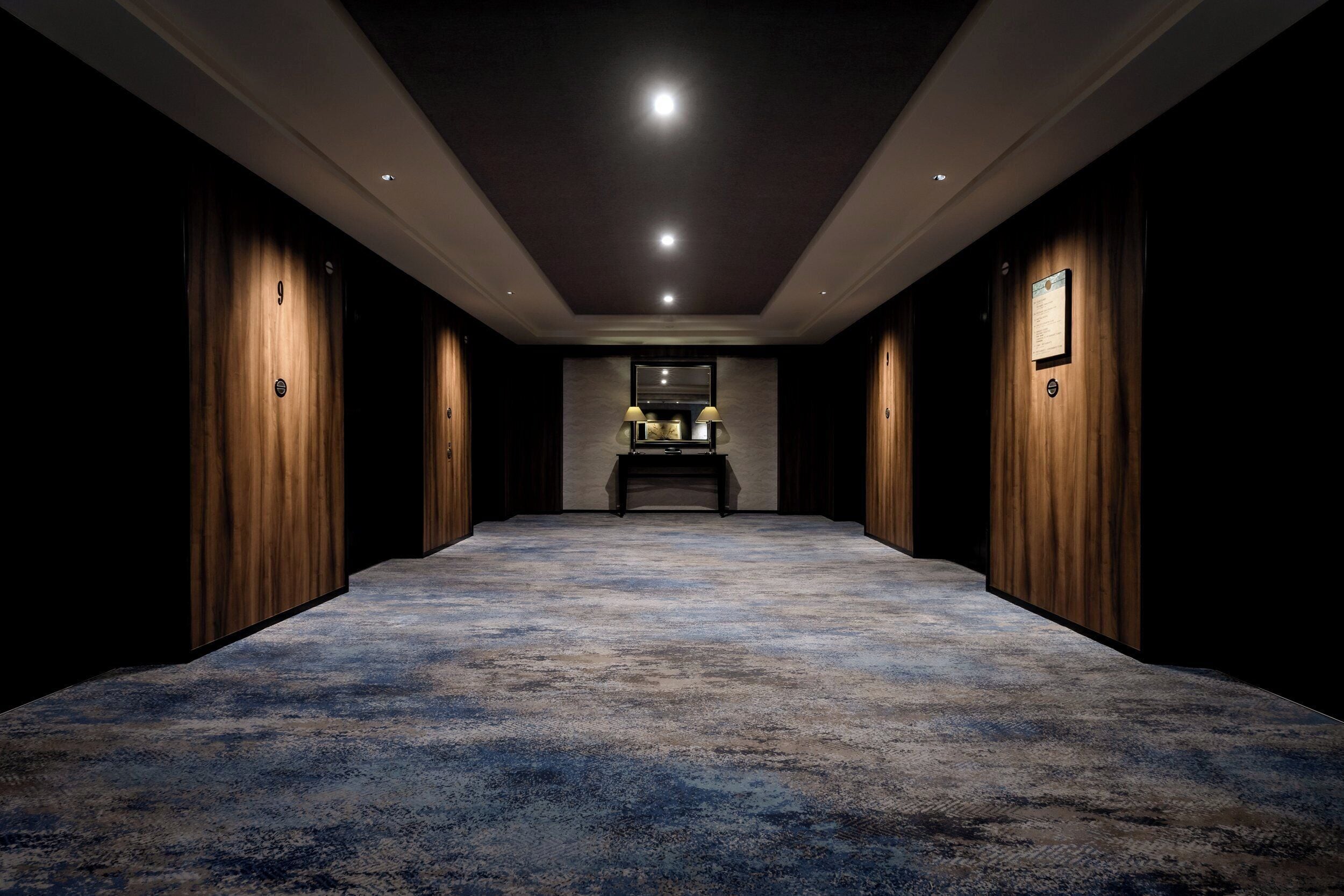 A hallway with a carpeted floor, wooden paneling on the walls, and a reception desk at the end.
