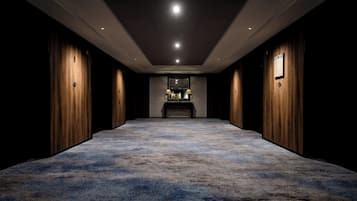 A hallway with a carpeted floor, wooden paneling on the walls, and a reception desk at the end.