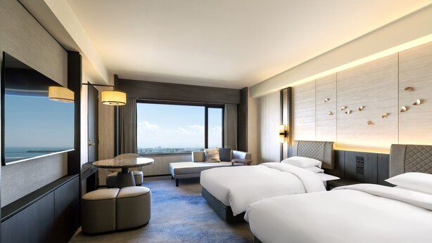 Una habitación de hotel moderna con una cama grande, zona de estar con una mesa y vistas a la ciudad.
