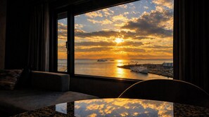 A room with a large window overlooking a sunset over a body of water, a sofa, and a small table. - Grand Prince Hotel Osaka Bay (Osaka)