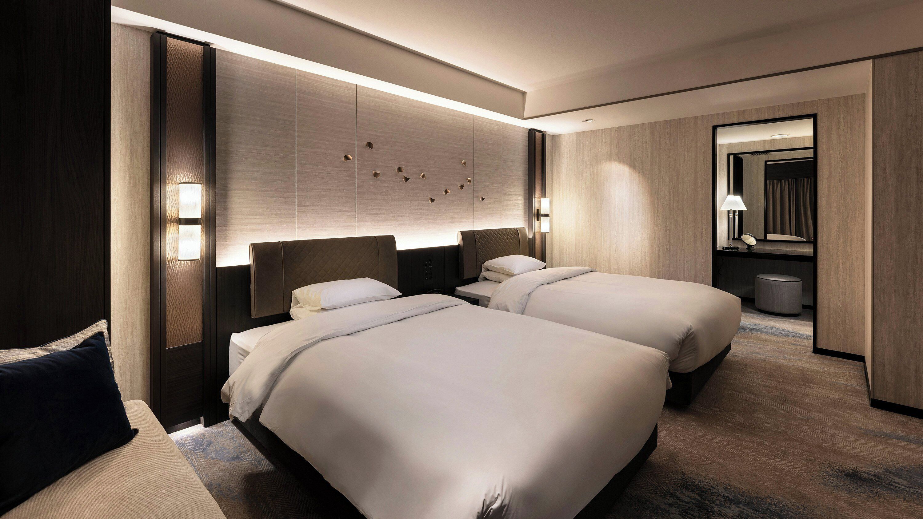 A modern hotel room with two beds, a large mirror, and a wall-mounted light fixture.