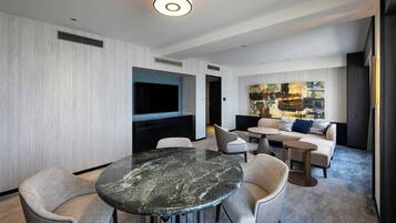 Une chambre d’hôtel moderne avec une table à manger en marbre, des sièges confortables, un téléviseur à écran plat et un grand tableau abstrait accroché au mur.
