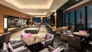 Un moderno vestíbulo de hotel con una amplia zona de comedor, asientos cómodos y grandes ventanales con vistas a la ciudad.