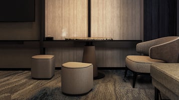 Une pièce moderne avec une table ronde, deux poufs, un canapé et une lampe suspendue.
