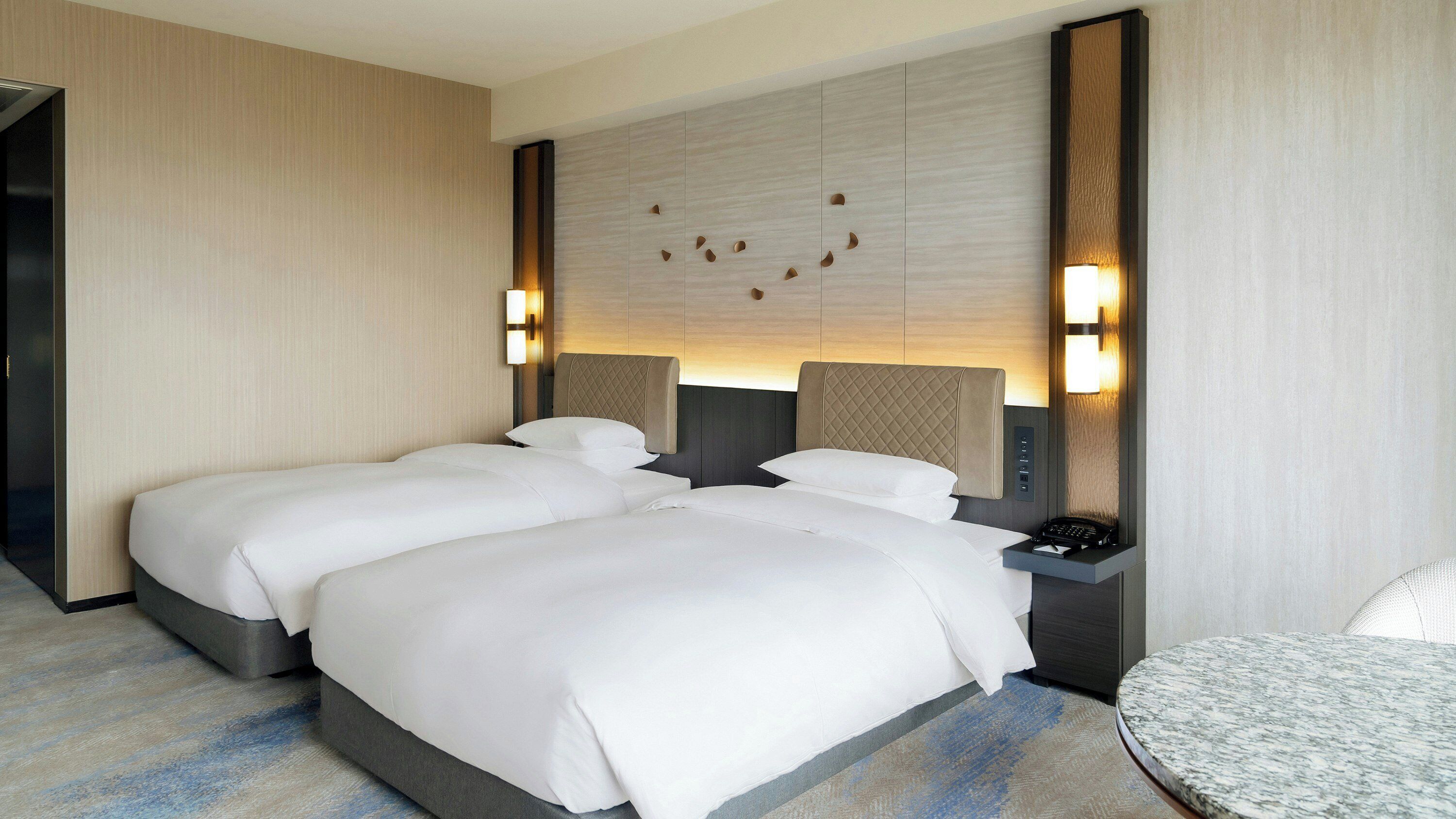 Une chambre d’hôtel avec deux lits, une table de chevet avec un téléphone et un luminaire fixé au mur.