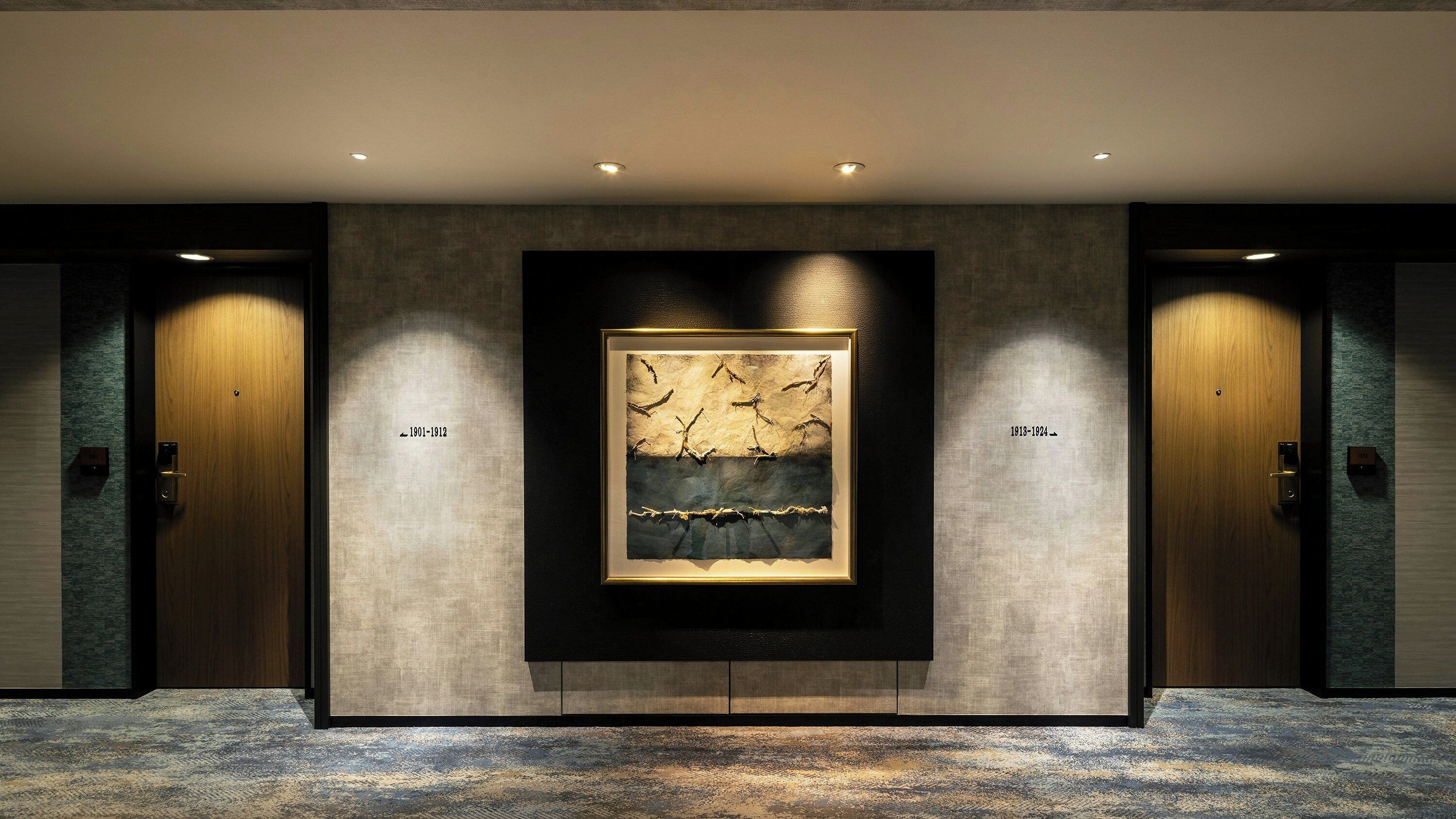 A hallway with a framed artwork on the wall, two wooden doors, and a carpeted floor.