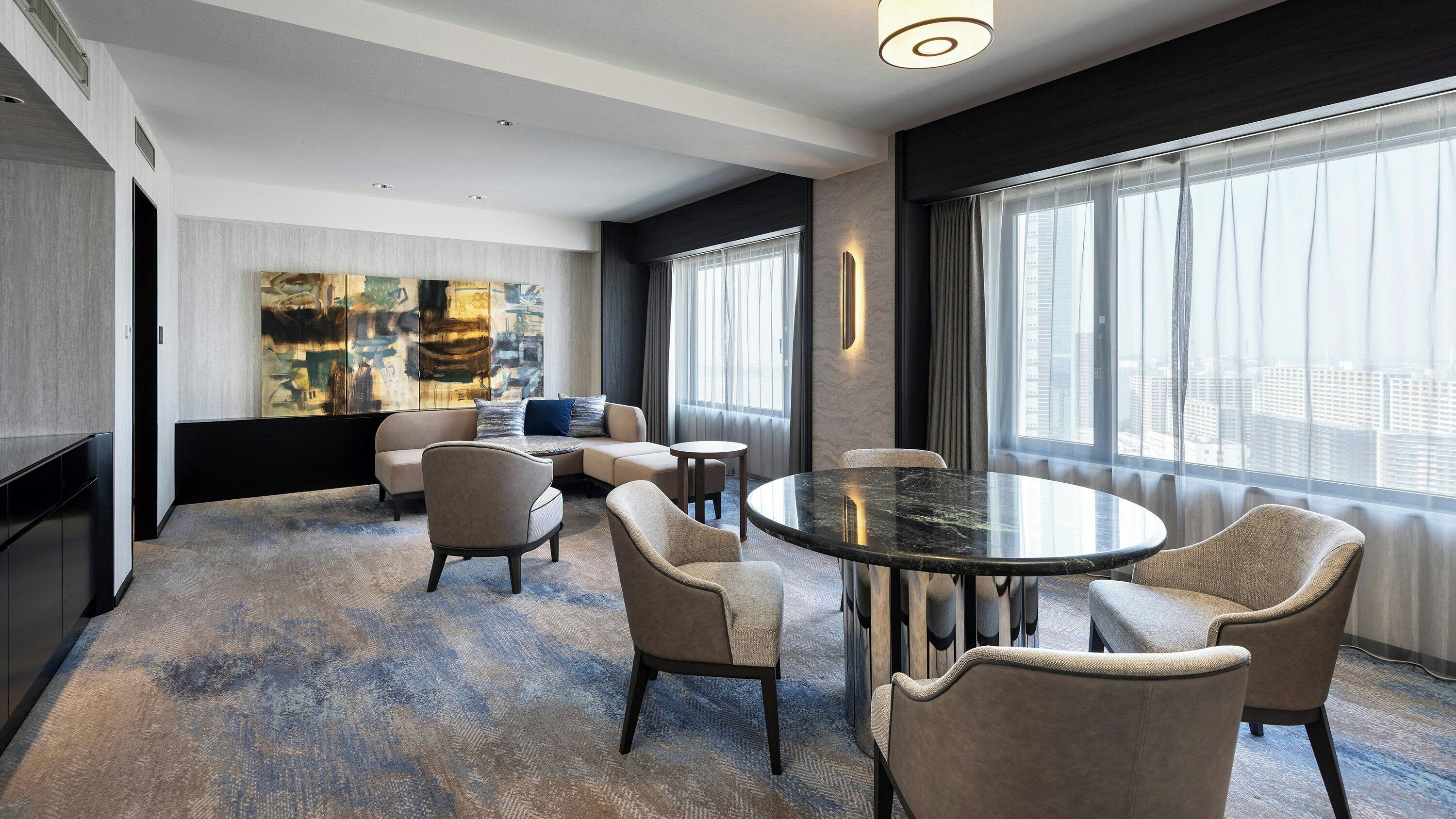 Quarto de hotel moderno com uma janela grande, uma mesa redonda e um sofá.