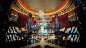 Un lobby espacioso con una imponente escalera en espiral, pisos de mármol y una gran escultura iluminada.