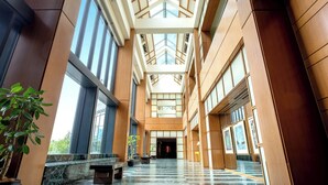 Un vestíbulo amplio con techos altos, ventanas grandes y una escalera central.