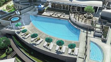 Une piscine sur le toit, dotée de chaises longues et de parasols, et entourée d’un bâtiment moderne à l’architecture arrondie.