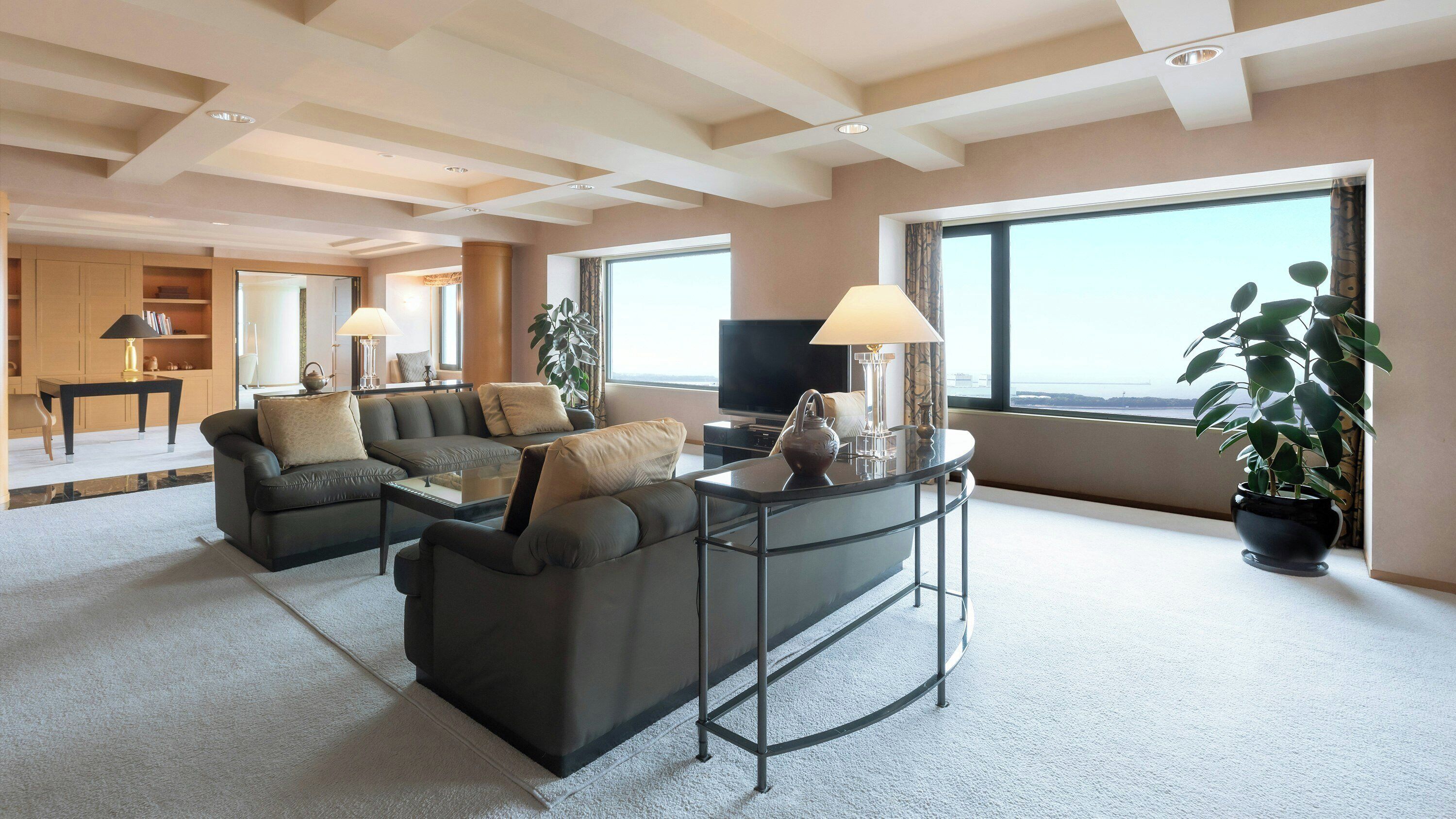 A modern living room with a sofa set, a coffee table, and a television. There is a large window providing a view of the outdoors.