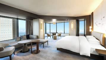 A modern hotel room with a large bed, a seating area with a round table, and a view of the cityscape through large windows.