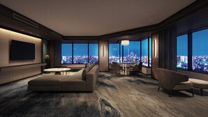 Una habitación de hotel moderna con un ventanal grande que ofrece vistas a la ciudad, un sofá cómodo, un comedor y un televisor de pantalla plana.