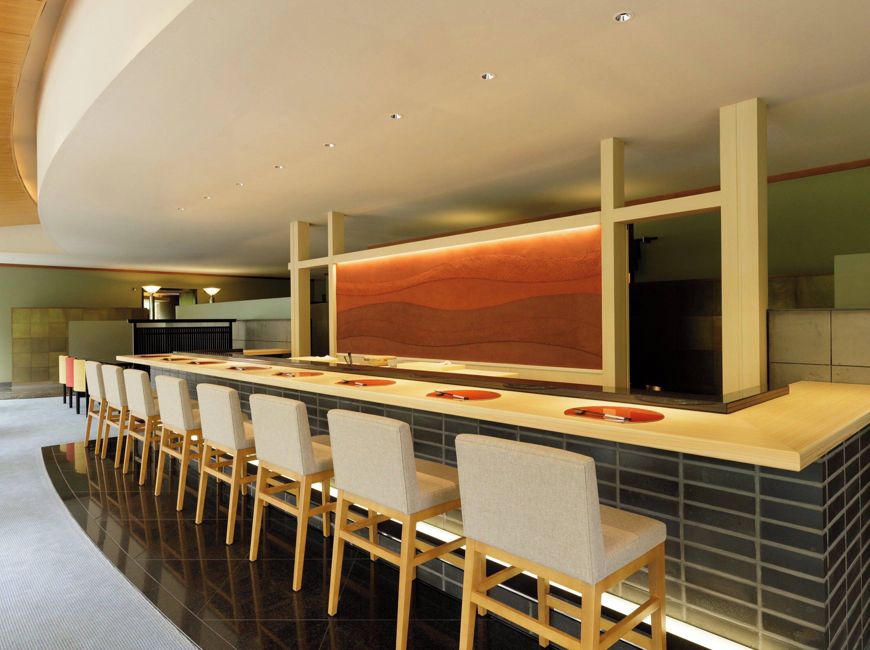 A modern bar area with a long counter, multiple bar stools, and a large illuminated wall feature.