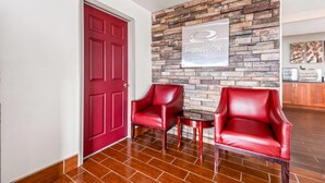 A reception area with a red door, two red leather chairs, a small table, and a stone wall with a sign reading "EconoLodge by Choice Hotel".